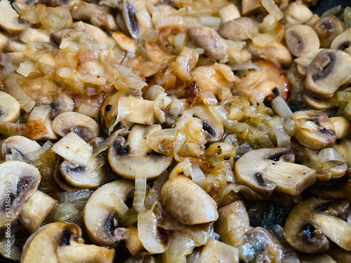 White champignon mushrooms are fried with onions in a frying pan.