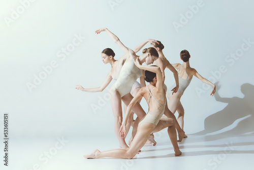 Group of young women, ballerinas dancing, performing isolated over grey studio background. Expression and flexibility