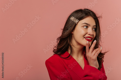 Close-up of beautiful young caucasian girl looking off to side on pink background with place of dough. Brunette girl with wavy hair is wearing red jacket. Lifestyle, leisure concept. 