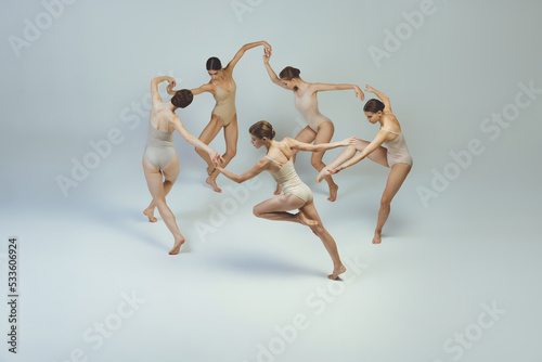 Group of young girls, ballet dancers performing, posing isolated over grey studio background. Circle movements