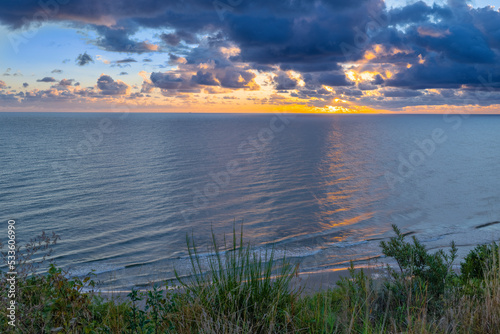Sunrise at Baltic Sea beach. Cloudy weather  small waves  no people. Sun flares and water reflection