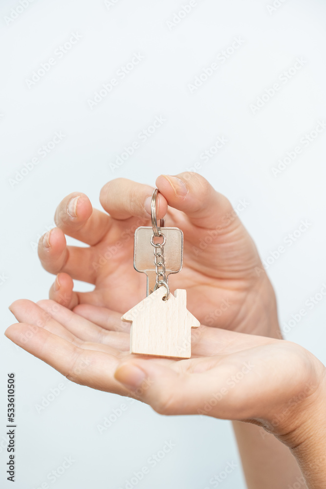 Close-up of beautiful hands of a woman with the new home keys. Keychain in the shape of a wooden house on white background. Close-up of beautiful hands of a woman with the new home keys. Keychain in the shape of a wooden house on white background.