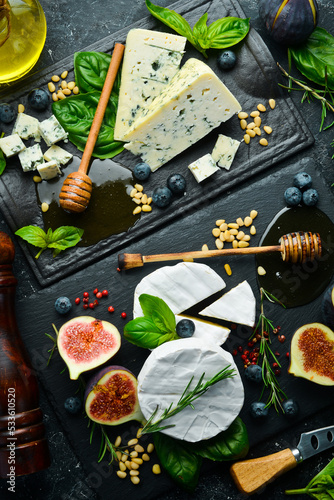 Assortment of cheese and snacks on stone black plates. Top view. On a black background.
