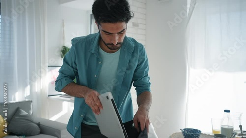 Young man hurrying up to work,finishing breakfast, taking laptop.