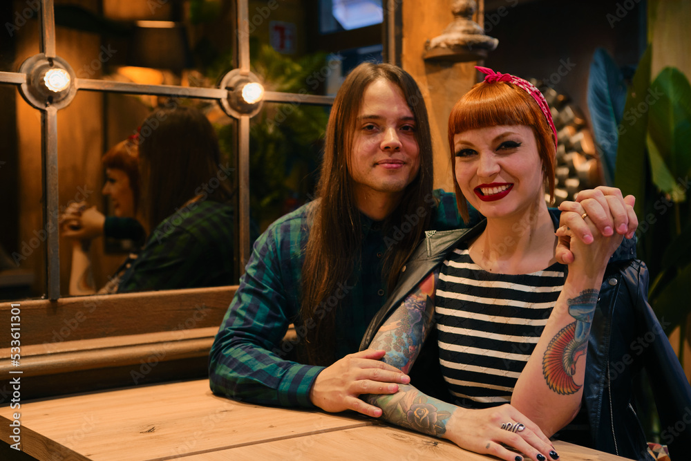 Smiling couple in a coffee shop looking at camera. She is red-haired and has a pin-up style