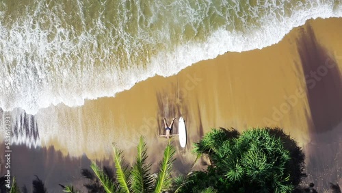4K drone shooting from above showing man prostrated on beach after intense surfing session. Surfing, active lifestyle, spending time at beach, exotic warm countries concept.