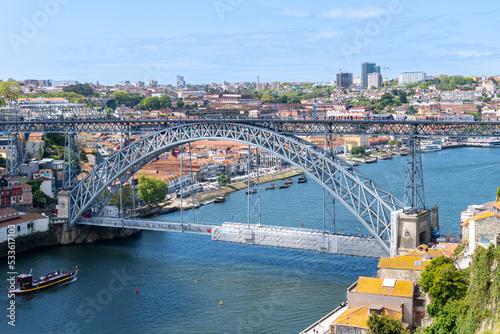 Don Luis I Bridge in Porto, with a part scaffolded for works, on a sunny day, with a ravelo sailing along the river.