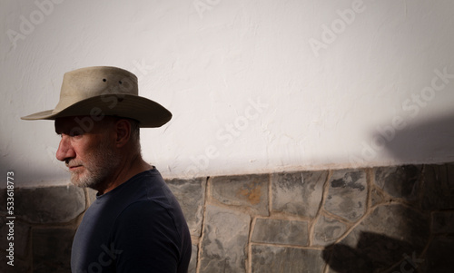 Portrait of adult man in cowboy hat against white wall with sunlight and shadow