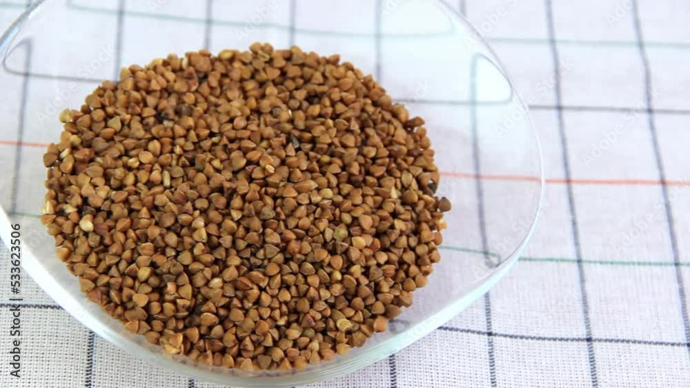 small grains of brown buckwheat in a transparent plate on a white background, the video image moves from right to left small grains of brown buckwheat in a transparent plate on a white background, the video image moves from right to left