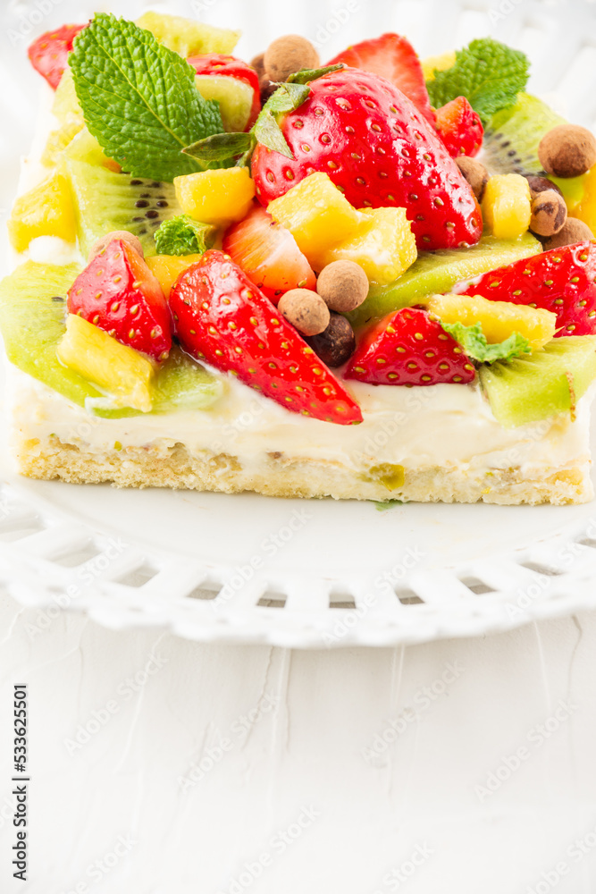 Close-up of fruit tart with strawberries, mango and kiwi, on a white plate, white table, vertical, with copy space Close-up of fruit tart with strawberries, mango and kiwi, on a white plate, white table, vertical, with copy space