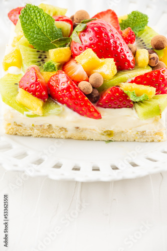 Fototapeta Naklejka Na Ścianę i Meble -  Close-up of fruit tart with strawberries, mango and kiwi, on a white plate, white table, vertical, with copy space