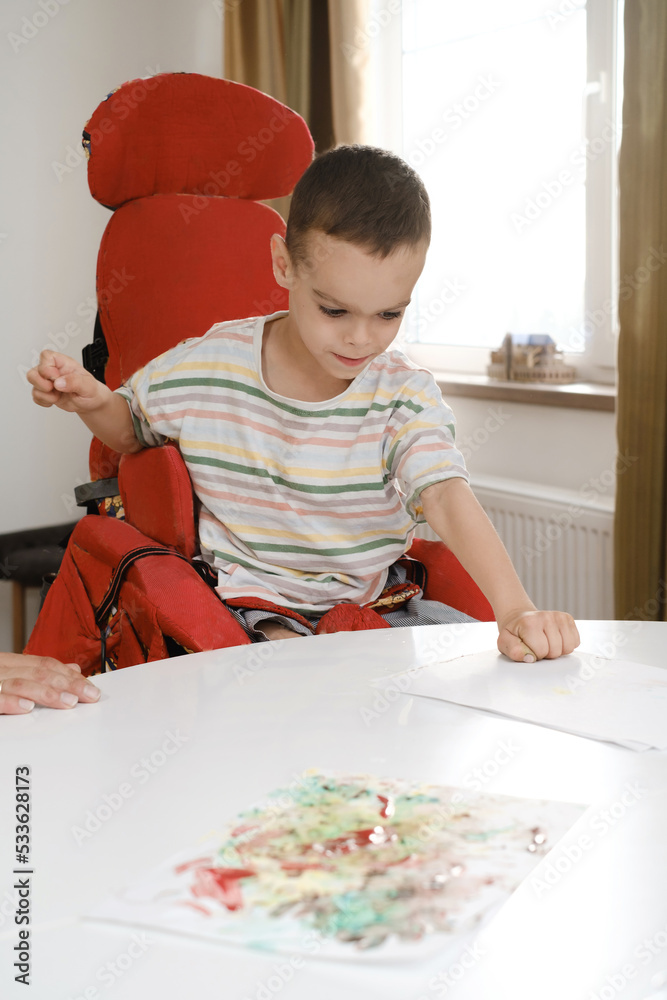 Child with cerebral palsy painting with fingers and hands. Happy