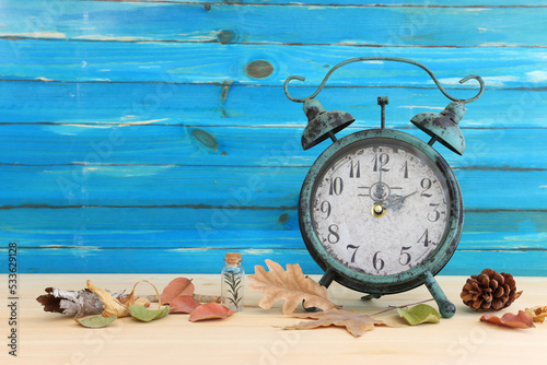 Image of autumn Time Change. Fall back concept. Dry leaves and vintage alarm Clock on rustic wooden table photo