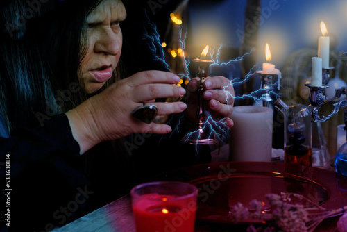 Canvas Print female witch holds candle in candlestick in her hands, conjures in dark room, ma