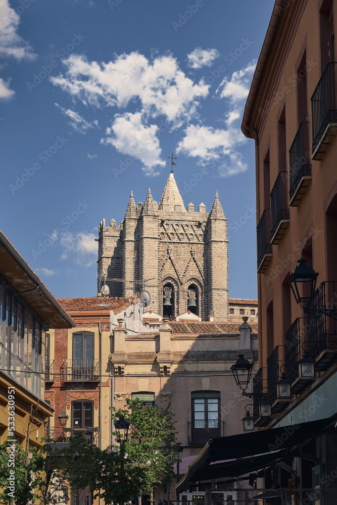 View of tower of cathedral from old street in old city in Avila, Spain with blue sky and clouds