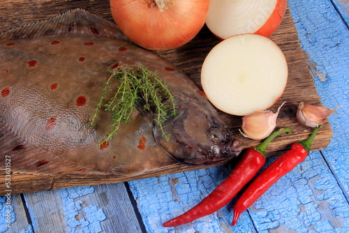 Fresh sea fish plaice (Pleuronectes platessa) on a wooden board decorated with onions, garlic and spices. Blue wooden plank background photo