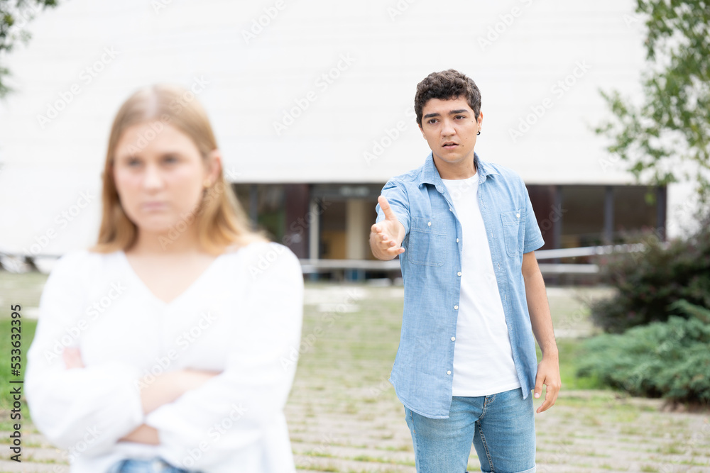 Hispanic teenager boy imploring forgiveness to girlfriend after breakup. Sad and angry girl leaving boyfriend. Hispanic teenager boy imploring forgiveness to girlfriend after breakup. Sad and angry girl leaving boyfriend.