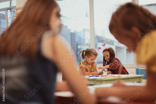 Creative kids during an art class in a daycare center or elementary school classroom drawing with female teacher. 