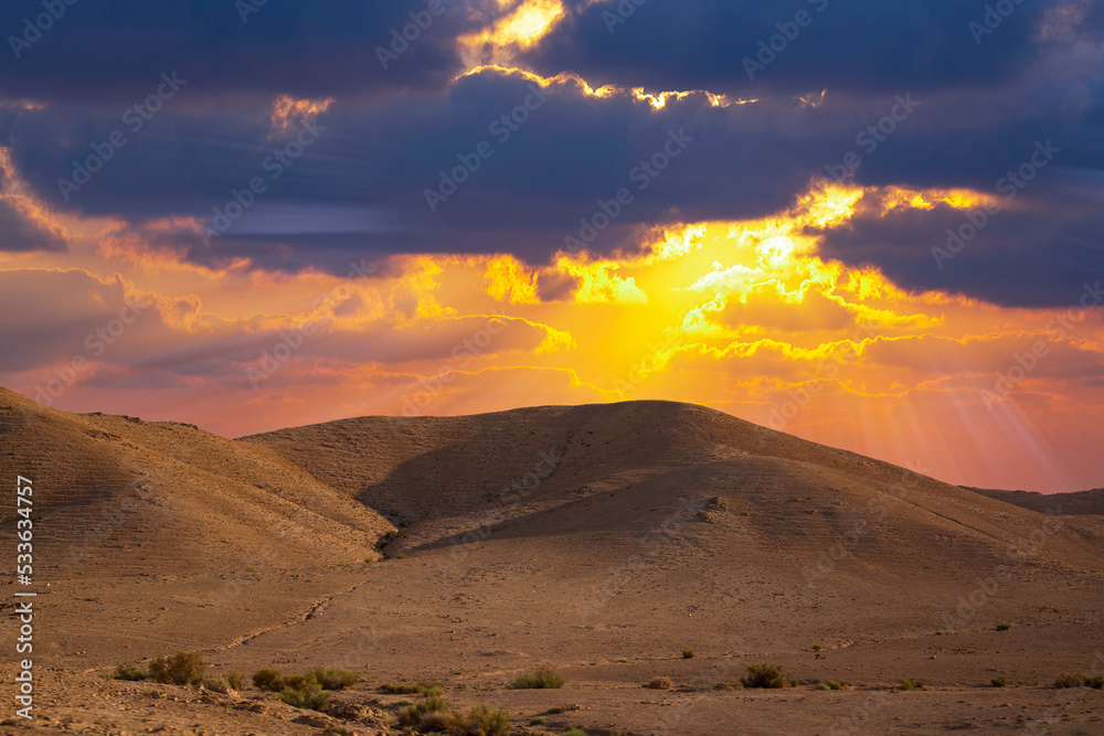 Yellow sunset in the desert and sun rays spreading. Beautiful dramatic clouds on gold sky. Golden sand dunes in desert in Judean desert, Israel. Sunny sky over cliffs, mountains Sodom and Gomorrah