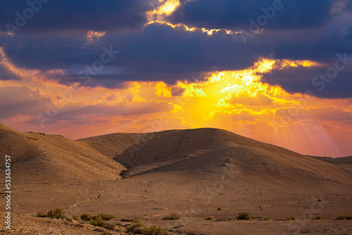 Yellow sunset in the desert and sun rays spreading. Beautiful dramatic clouds on gold sky. Golden sand dunes in desert in Judean desert, Israel. Sunny sky over cliffs, mountains Sodom and Gomorrah