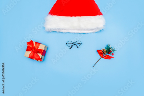 A Christmas card made of a Santa Claus hat, Santa glasses, a New Year's gift, branches of a fir tree on a blue background. Top view, place for text, copy space