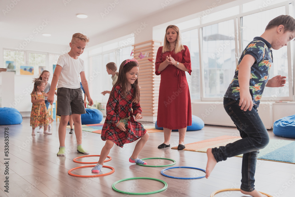 Small nursery school children with female teacher on floor indoors in  classroom, doing exercise. Jumping over hula hoop circles track on the  floor. foto de Stock | Adobe Stock