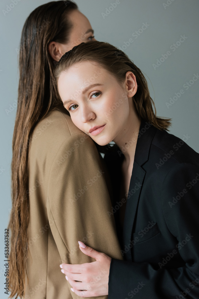 young lesbian woman looking at camera while leaning on long haired lesbian girlfriend isolated on grey. young lesbian woman looking at camera while leaning on long haired lesbian girlfriend isolated on grey.