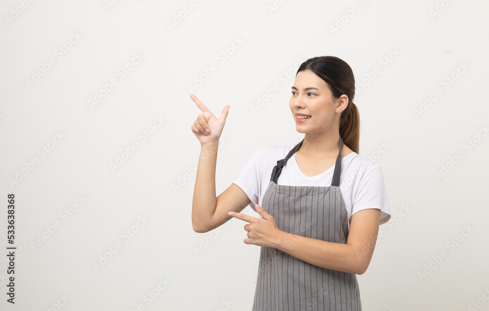 Young beautiful woman with apron standing on isolated white background pointing finger to blank space. Housekeeping housework or maid worker concept. Young beautiful woman with apron standing on isolated white background pointing finger to blank space. Housekeeping housework or maid worker concept.