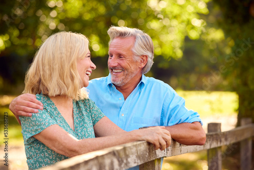 Smiling Casually Dressed Mature Or Senior Couple Leaning On Fence On Walk In Countryside