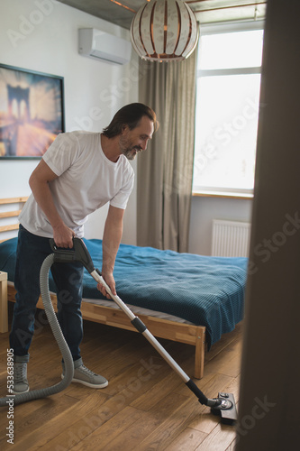 Man in white tshirt doing vacuum cleaning and looking involved