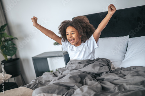 Cute curly-haired girl waking up in the mornign and feeling energized