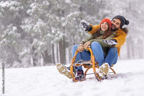 Couple sitting on sled and sliding down the hill while on winter vacation photo