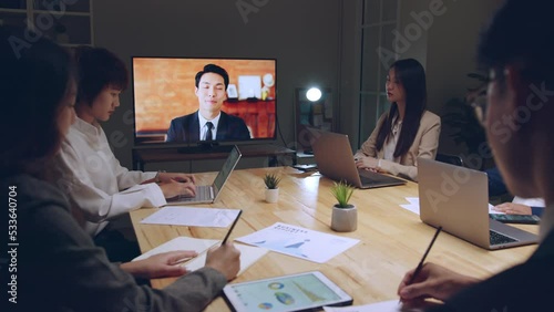 Business people group remote meeting with manager leader via video call conference virtual meeting on tv screen in office at night photo