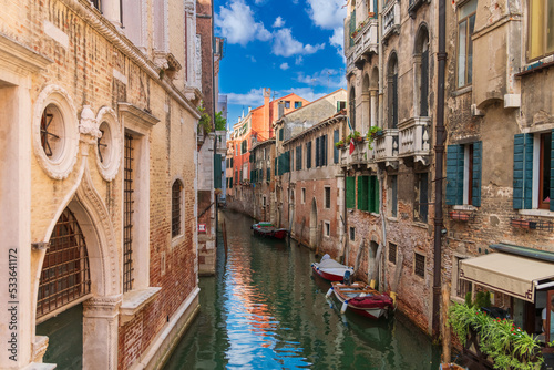 Boats near a vintage brick wall on the water surface of a narrow canal street in Venice, reflections of old houses with windows on a Venetian street, Venice canal on a sunny day © Александр Бочкала