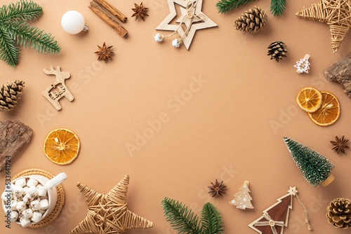 Top view photo of christmas decorations wood ornaments wicker stars cup of cocoa pine cones branches bark cinnamon dried orange slices on isolated beige background with copyspace in the middle