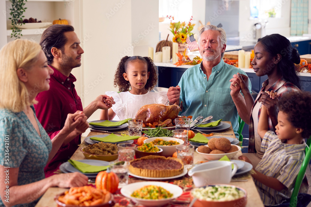 Multi-Generation Family Celebrating Thanksgiving At Home Saying Prayer Before Eating Meal Together