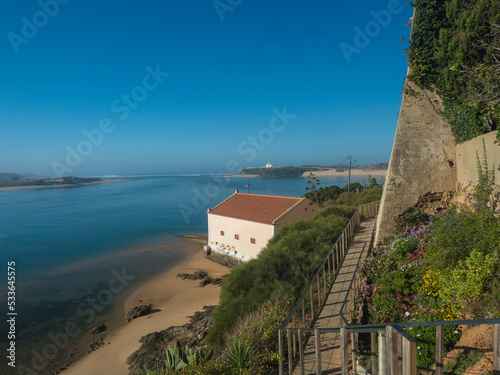 Idyllic view of the mouth of Mira river flowing into the Atlantic Ocean with stairs leading to port and ferry and small beach house. Vila Nova de Milfontes, Vicentine Coast Natural Park Portugal