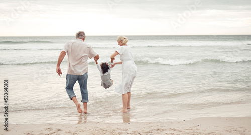 Family, children and beach with a girl and her grandparents by the sea or ocean in nature. Sand, water and summer with a senior man, woman and their granddaughter on holiday or vacation by the coast