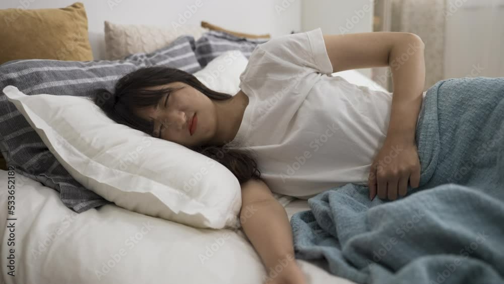 asian girl having severe cramp in lower abdomen is touching her belly and lying on bed with a painful look on face in the bedroom at home during daytime. asian girl having severe cramp in lower abdomen is touching her belly and lying on bed with a painful look on face in the bedroom at home during daytime.