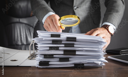 Businessman holding magnifying glass with documents.