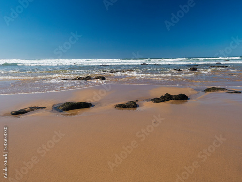 Fototapeta Naklejka Na Ścianę i Meble -  View of empty Praia do Brejo Largo beach with ocean waves and sharp rocks and wet golden sand at wild Rota Vicentina coast near Porto Covo, Portugal.