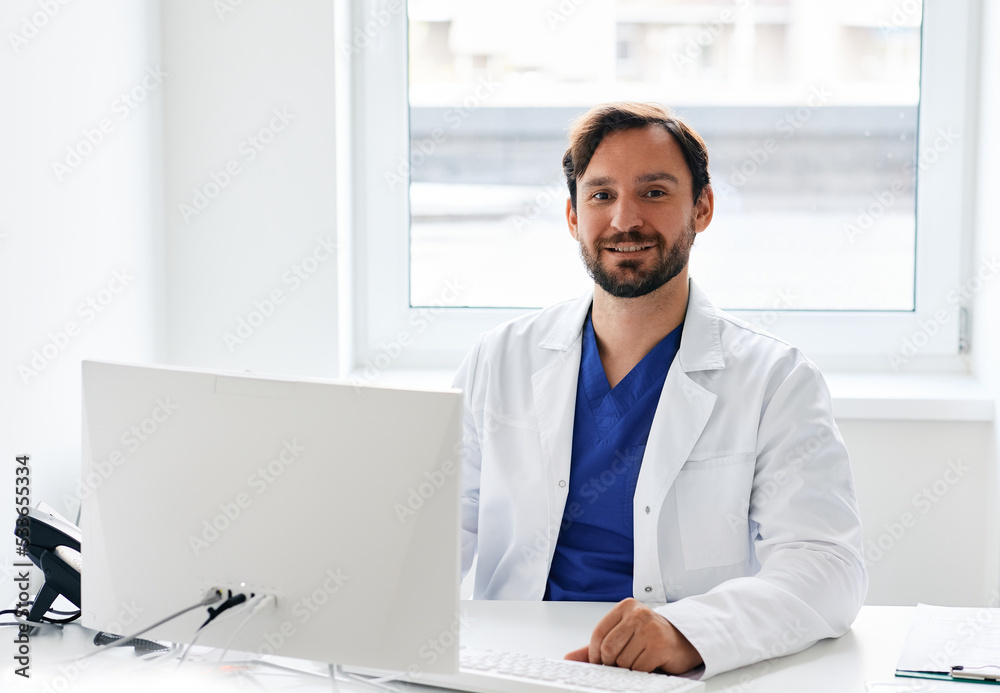 Obraz premium Portrait of smiling general practitioner wearing doctor's uniform sitting in his workplace office at medical clinic. Doctor's consultation