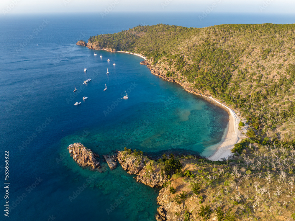 Evening aerial high angle drone view of Blue Pearl Bay on Hayman Island, the most northerly of the Whitsunday Islands in Queensland, Australia with sailing ships and yachts anchored near shore.