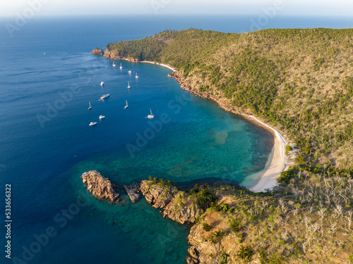 Evening aerial high angle drone view of Blue Pearl Bay on Hayman Island, the most northerly of the Whitsunday Islands in Queensland, Australia with sailing ships and yachts anchored near shore.
