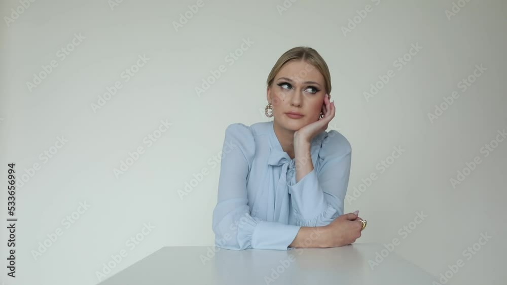 Bored, tired pretty, elegant blond woman in formal shirt sit at table and waiting for job interview on white background Bored, tired pretty, elegant blond woman in formal shirt sit at table and waiting for job interview on white background