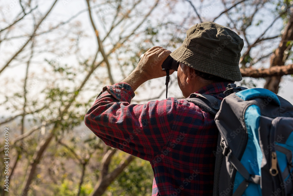 A man tourist exploring a forest and using professional binoculars