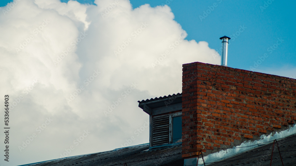 chimney on a roof and fluffy clouds in back. White clouds in the blue sky and the roof of a house with a chimney.