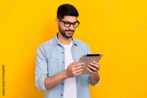 Portrait of young guy wear denim shirt holding tablet online education student isolated on bright yellow color background