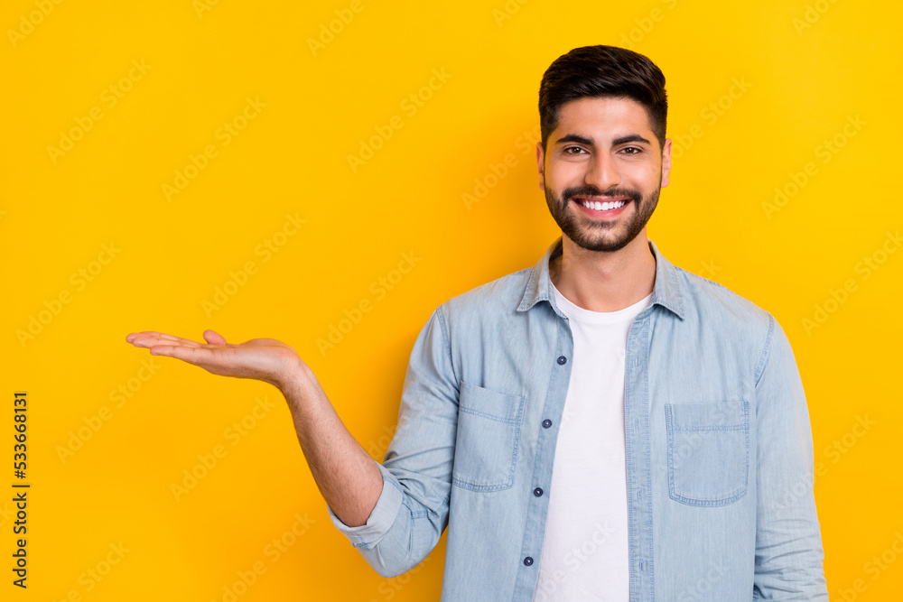 Photo of young smiling guy wear denim shirt holding expensive thing isolated on bright yellow color background Photo of young smiling guy wear denim shirt holding expensive thing isolated on bright yellow color background