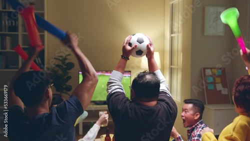 Happy Asian people with friends watching soccer or football on tv and celebrating victory at home, world cup football cheering concept